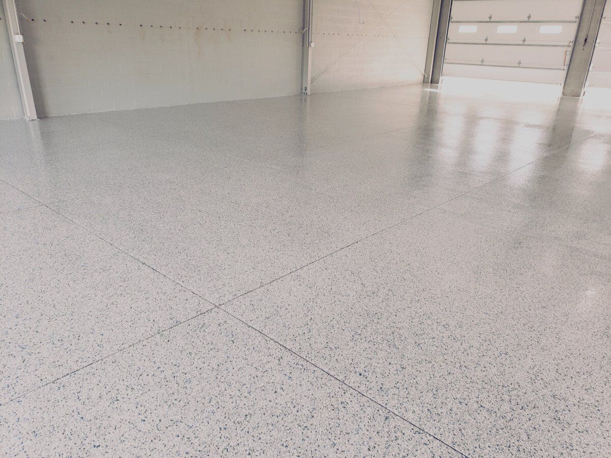 a white concrete floor in a garage with a garage door in the background .