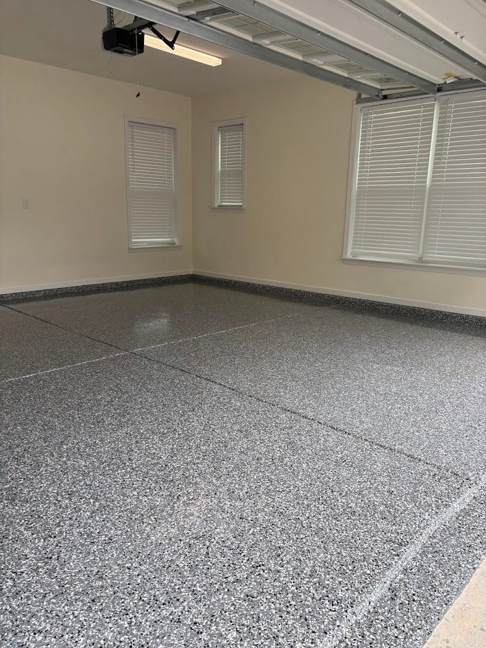 Grey speckled epoxy garage floor with beige walls and two windows.