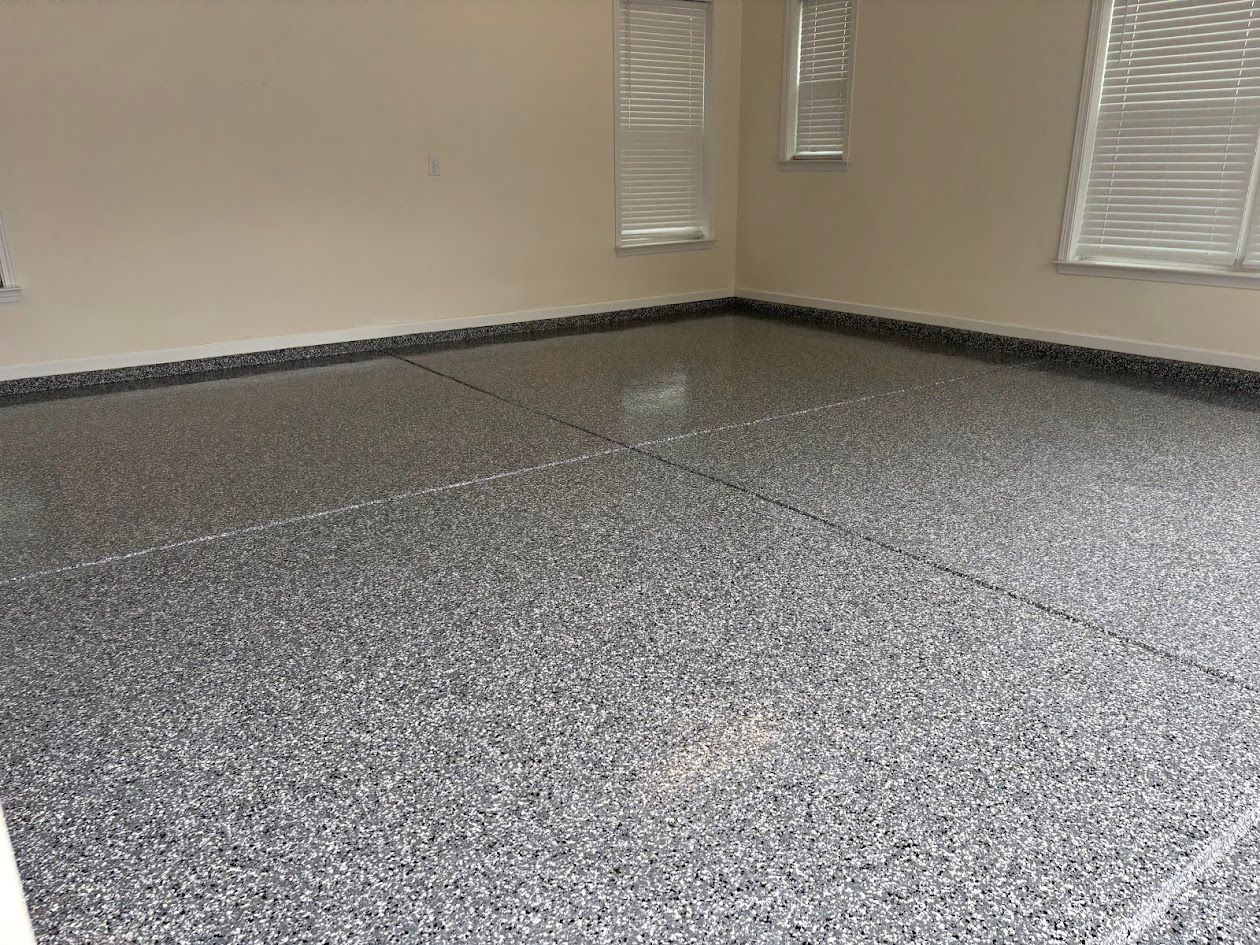 Garage floor with dark gray speckled epoxy coating. Windows with blinds are visible.
