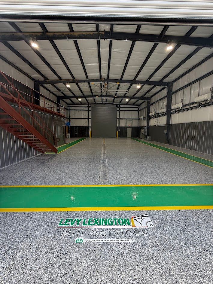 Interior of a large warehouse, with a green and gray speckled floor and a large gray door at the end.