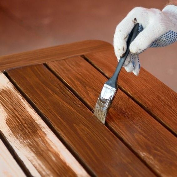 A person is painting a wooden table with a brush.