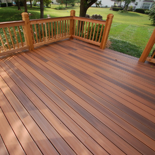 A wooden deck with a railing overlooking a lush green field