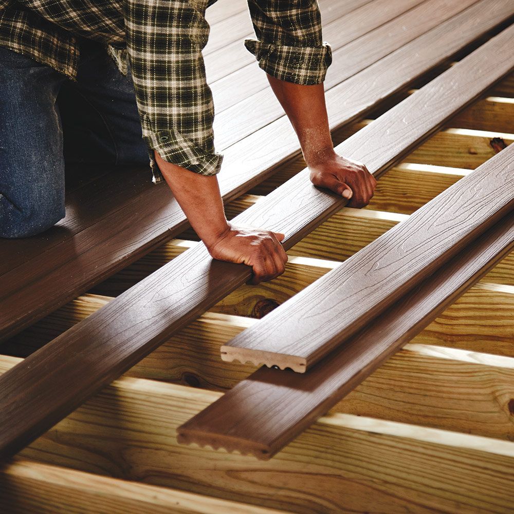 A man in a plaid shirt is working on a wooden deck