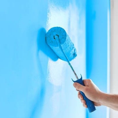 A person is painting a blue wall with a blue paint roller.