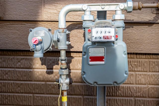 Gray gas meter attached to a brown brick wall.
