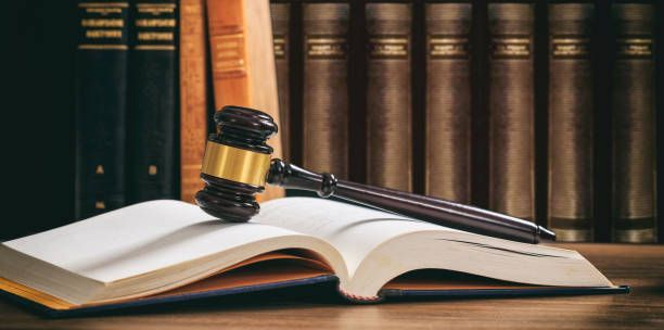 Gavel resting on an open book, with a row of books in the background.