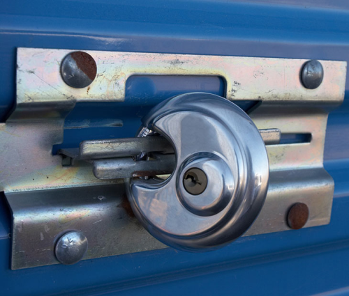 Close-up of a metal padlock securing a blue gate latch on a silver bracket.