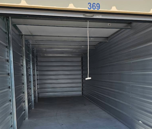 Empty gray storage unit with open roll-up door and number 369 above the entrance.