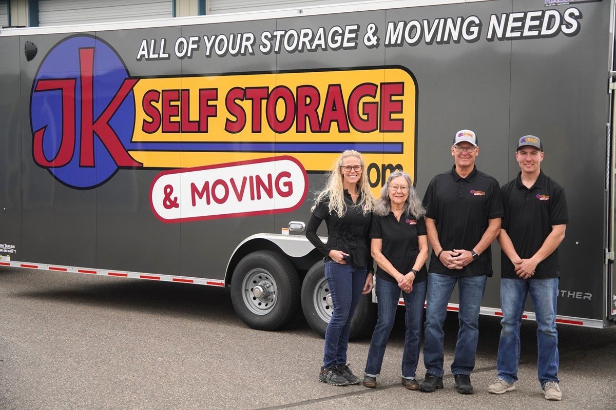 JK Self Storage & Moving truck and trailer with the family of owners standing beside it in professional clothing.