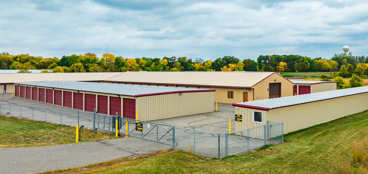 Scenic view of a storage facility with red doors, brown siding, a maintained lawn, and gated access