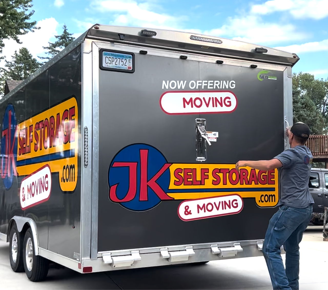 Moving truck with a JK Self Storage & Moving decal, loading a mattress into its trailer.