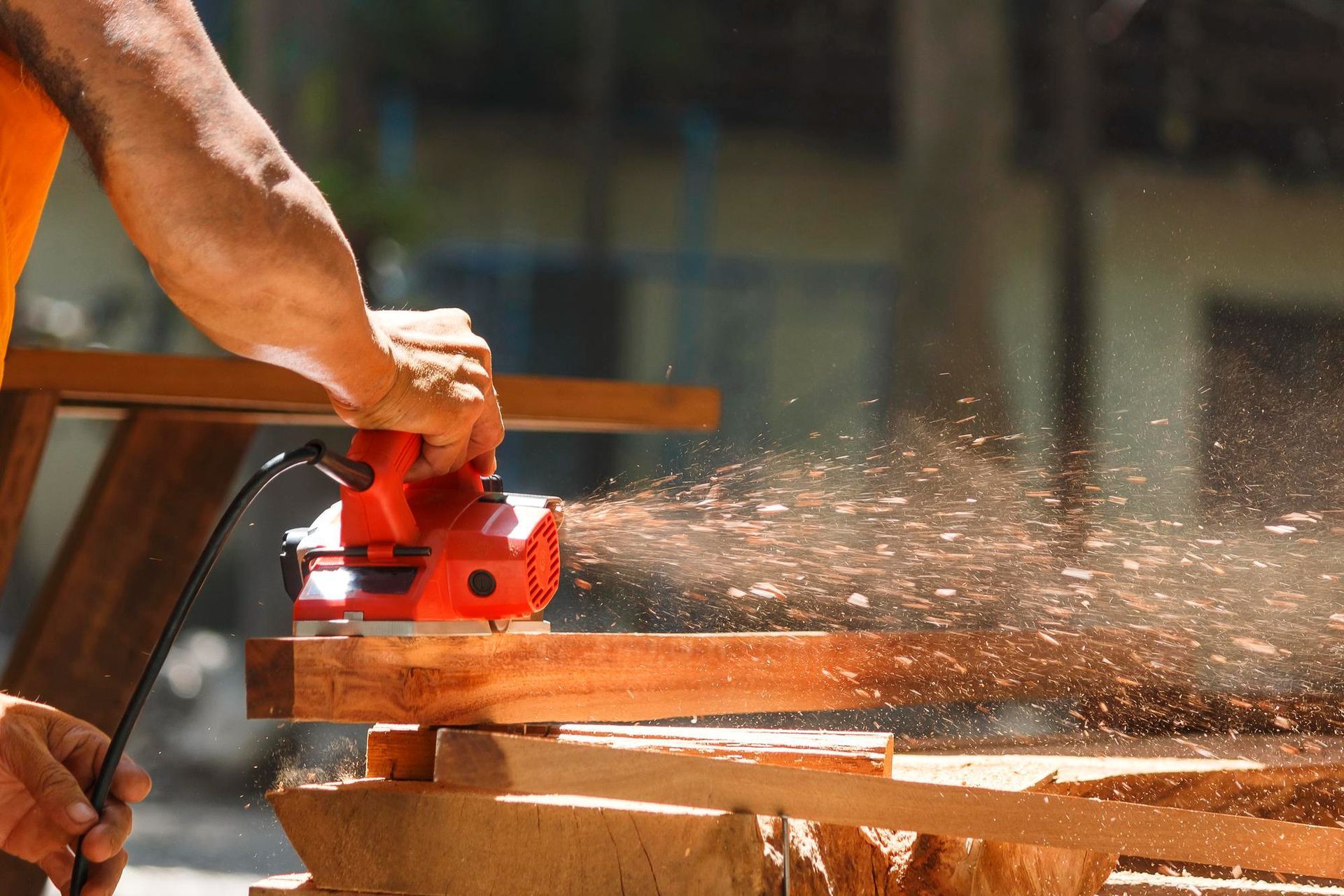 Person using a red circular saw to cut wood, with sawdust flying in a workshop