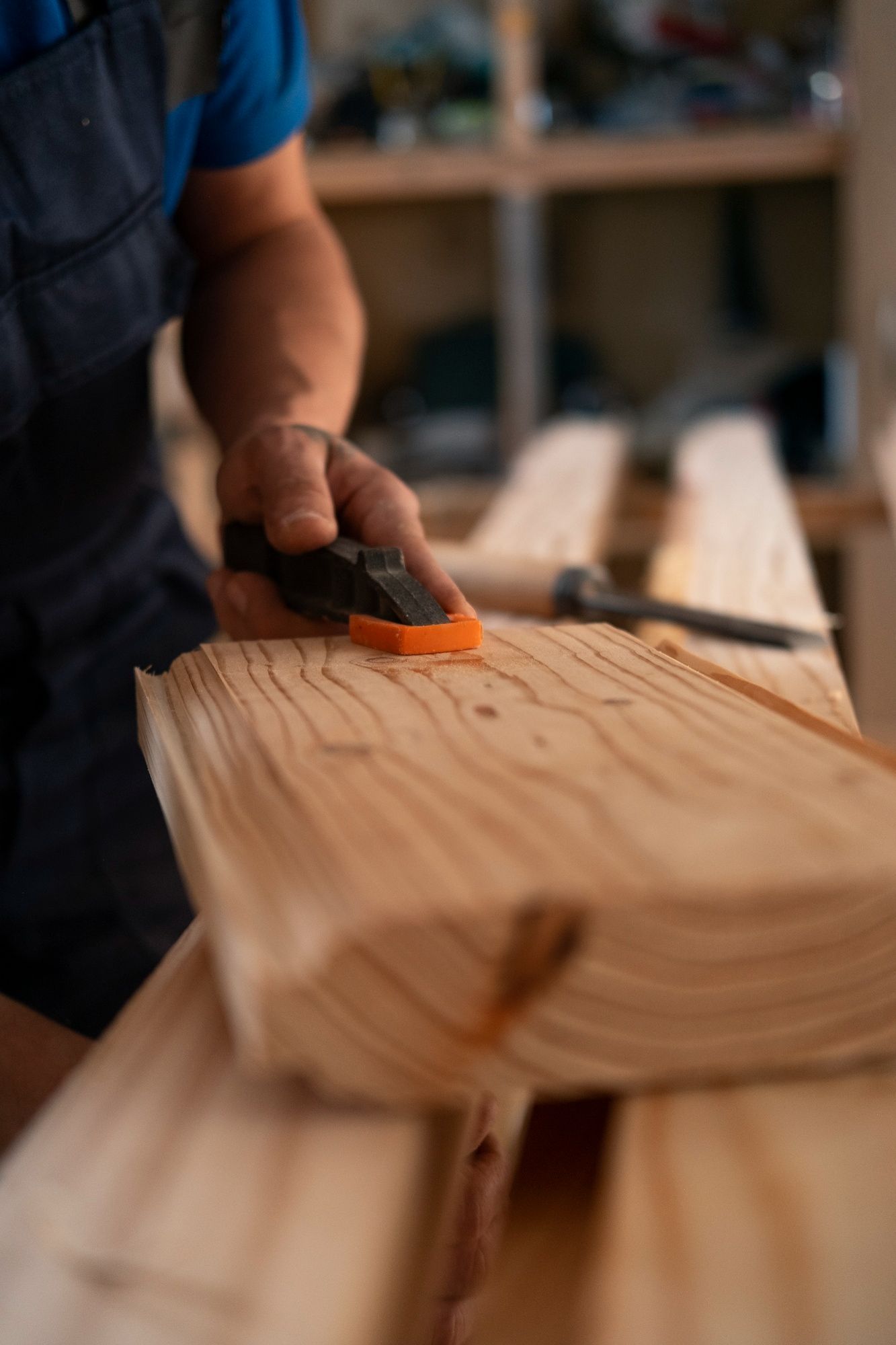 Hand sanding a wooden board in a workshop, with blurred lumber in the foreground
