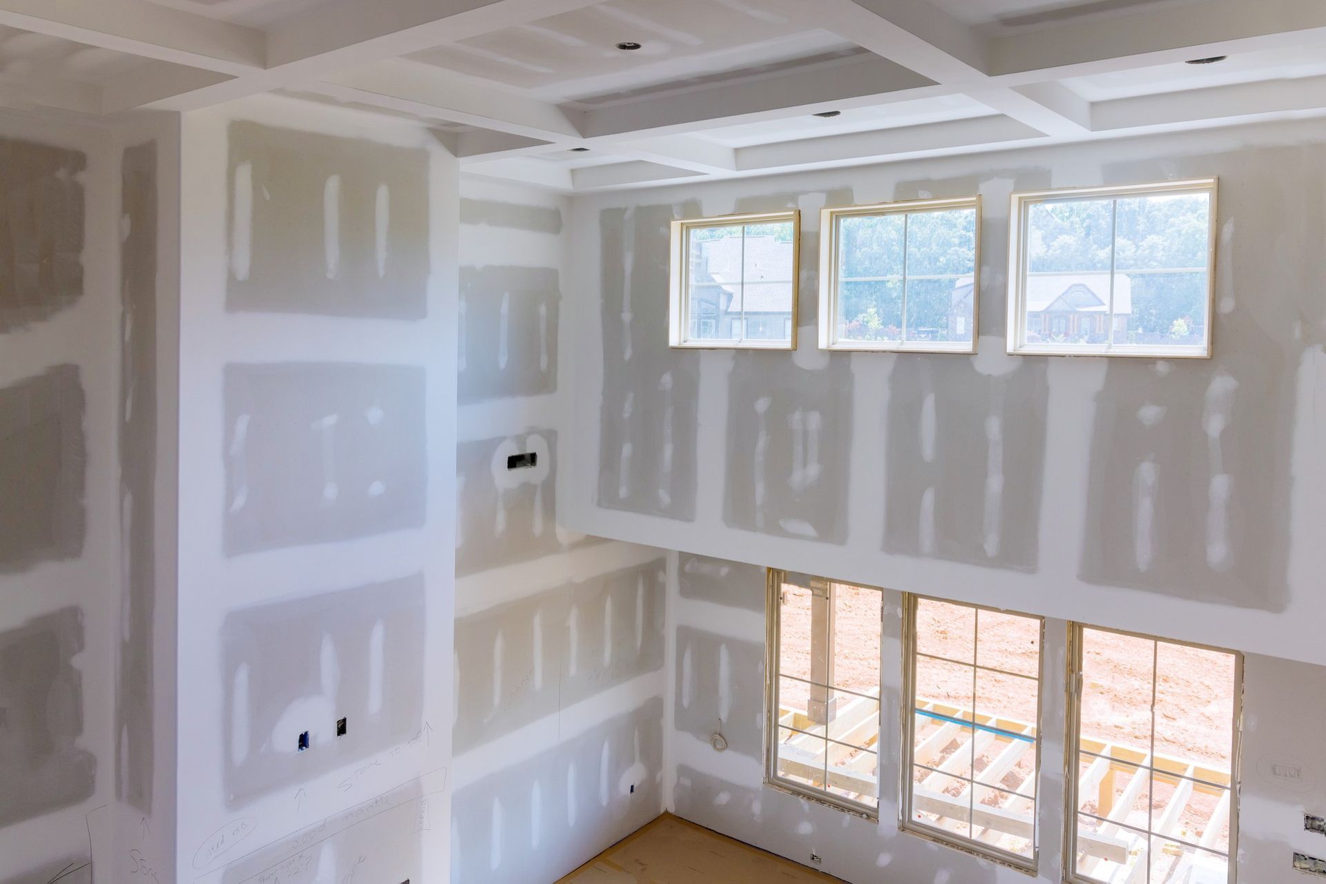 Unfinished drywall interior with taped seams and large windows letting in daylight.