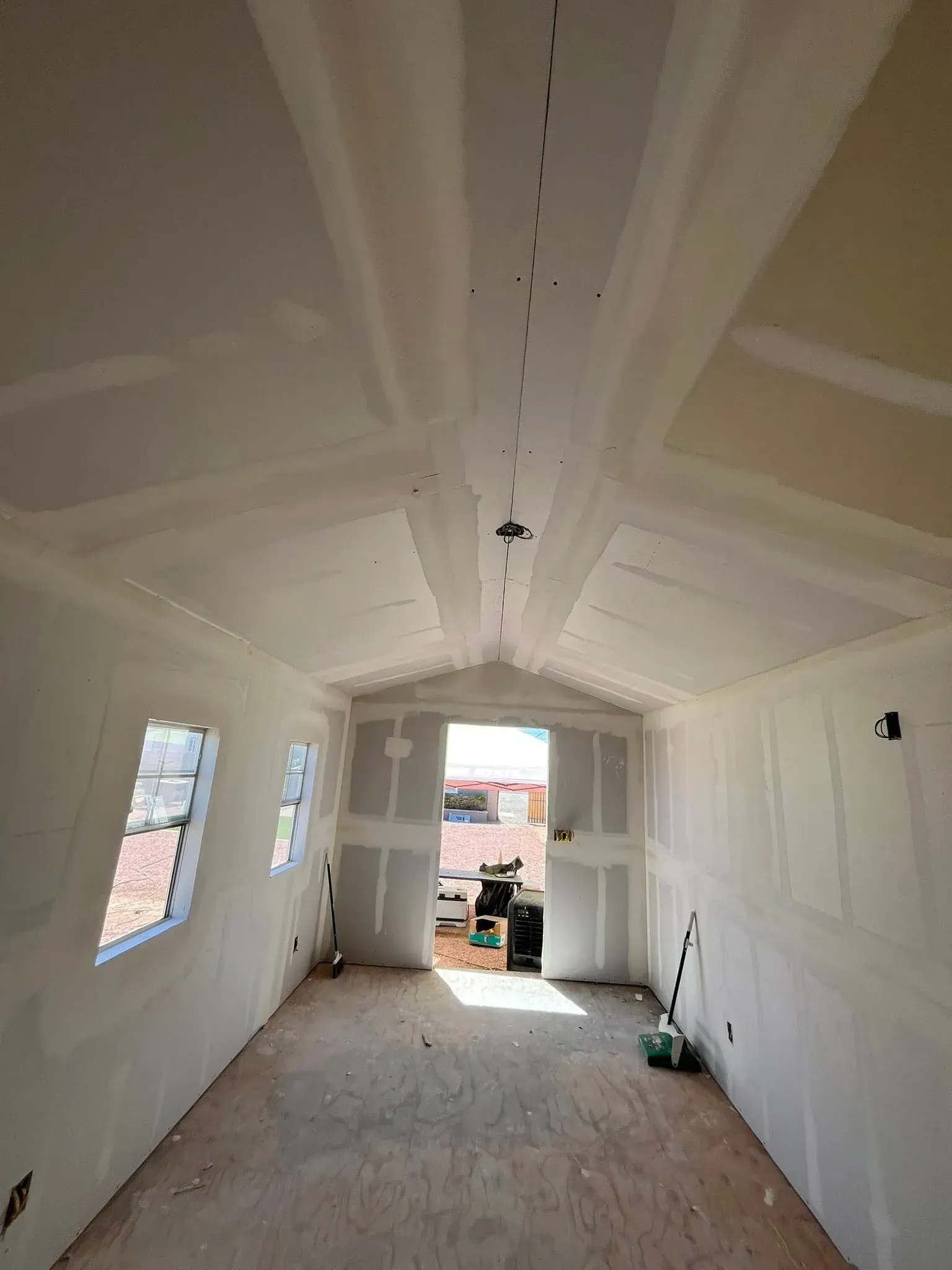 Drywall installation and finishing in progress inside a Tempe home with a vaulted ceiling and windows Drywall installation and finishing in progress inside a Tempe home with a vaulted ceiling and windows