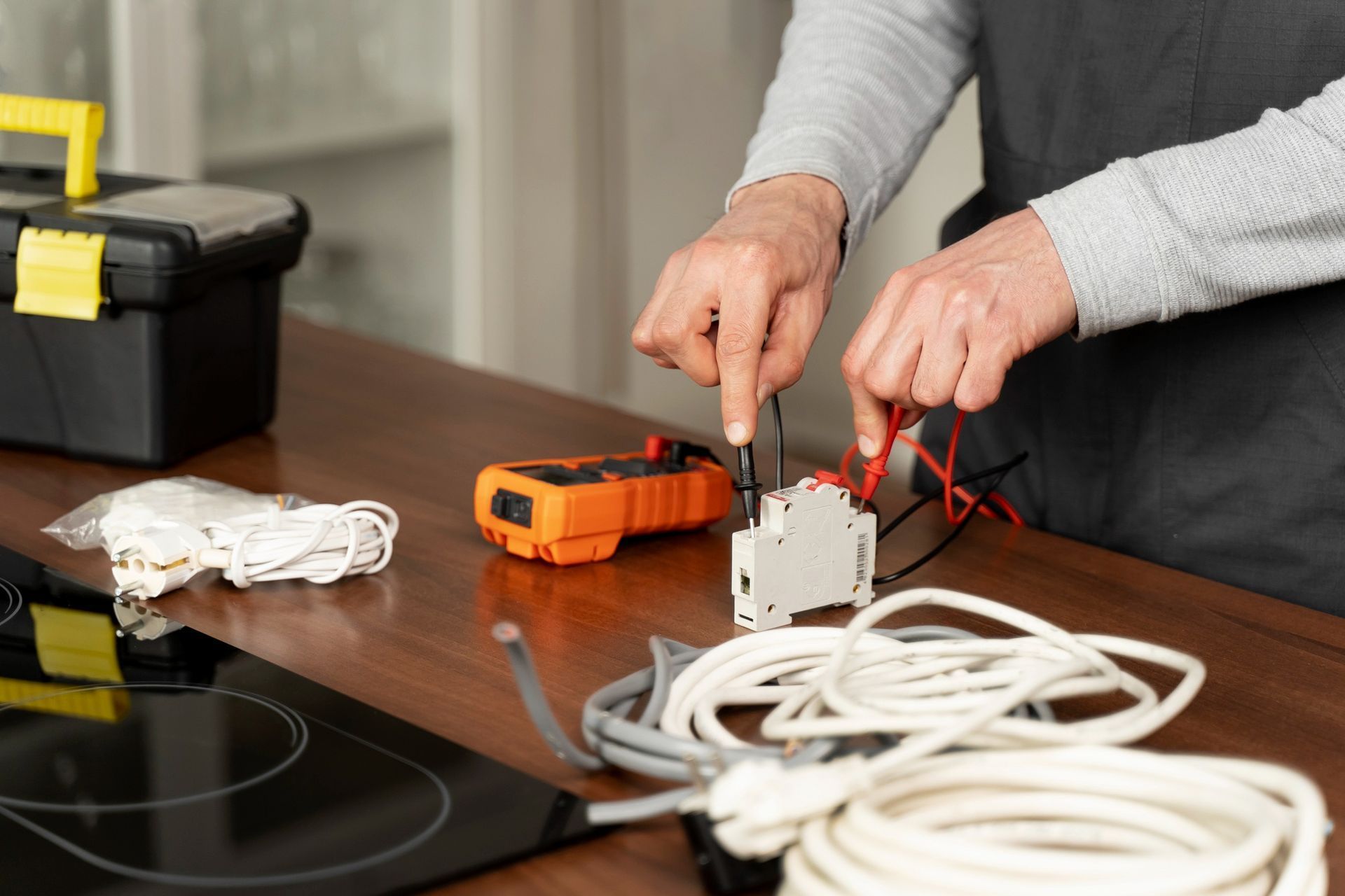 Hands wiring a white power strip on a wooden table with orange tool and coiled cables