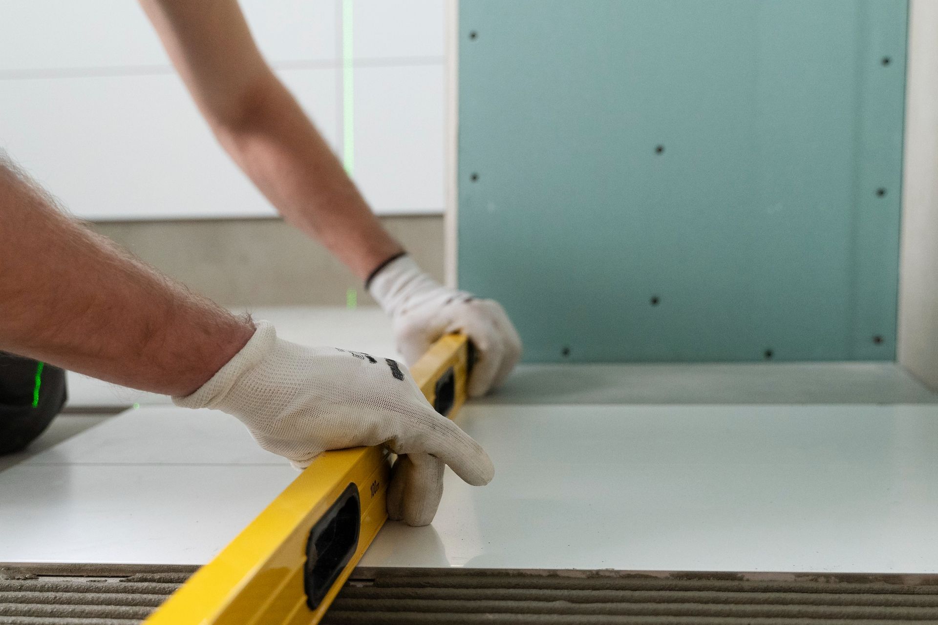 Gloved hands measuring a white board with a yellow level in a home renovation setting