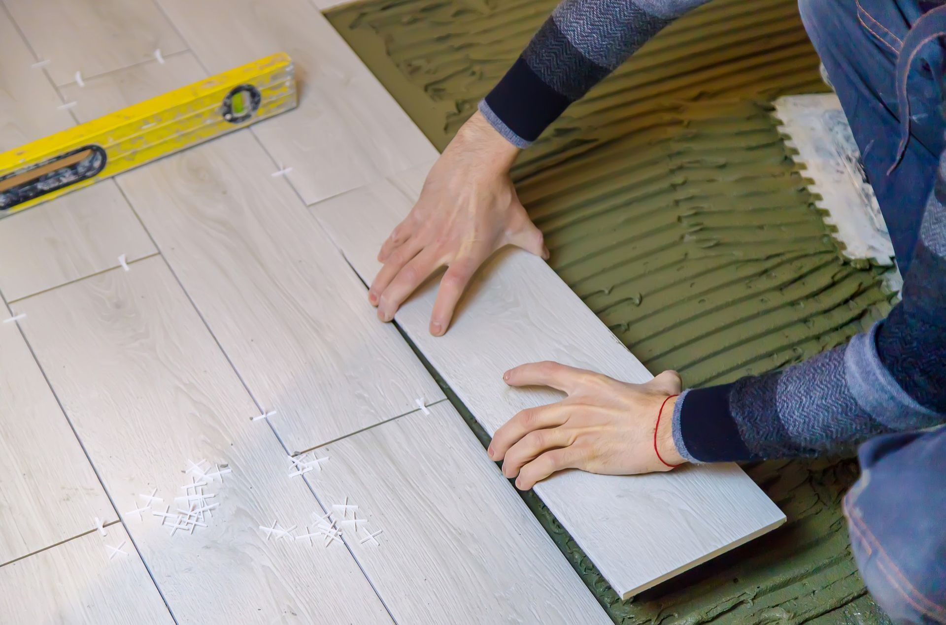 Hands laying white floor tiles with a yellow level nearby on a tiled floor