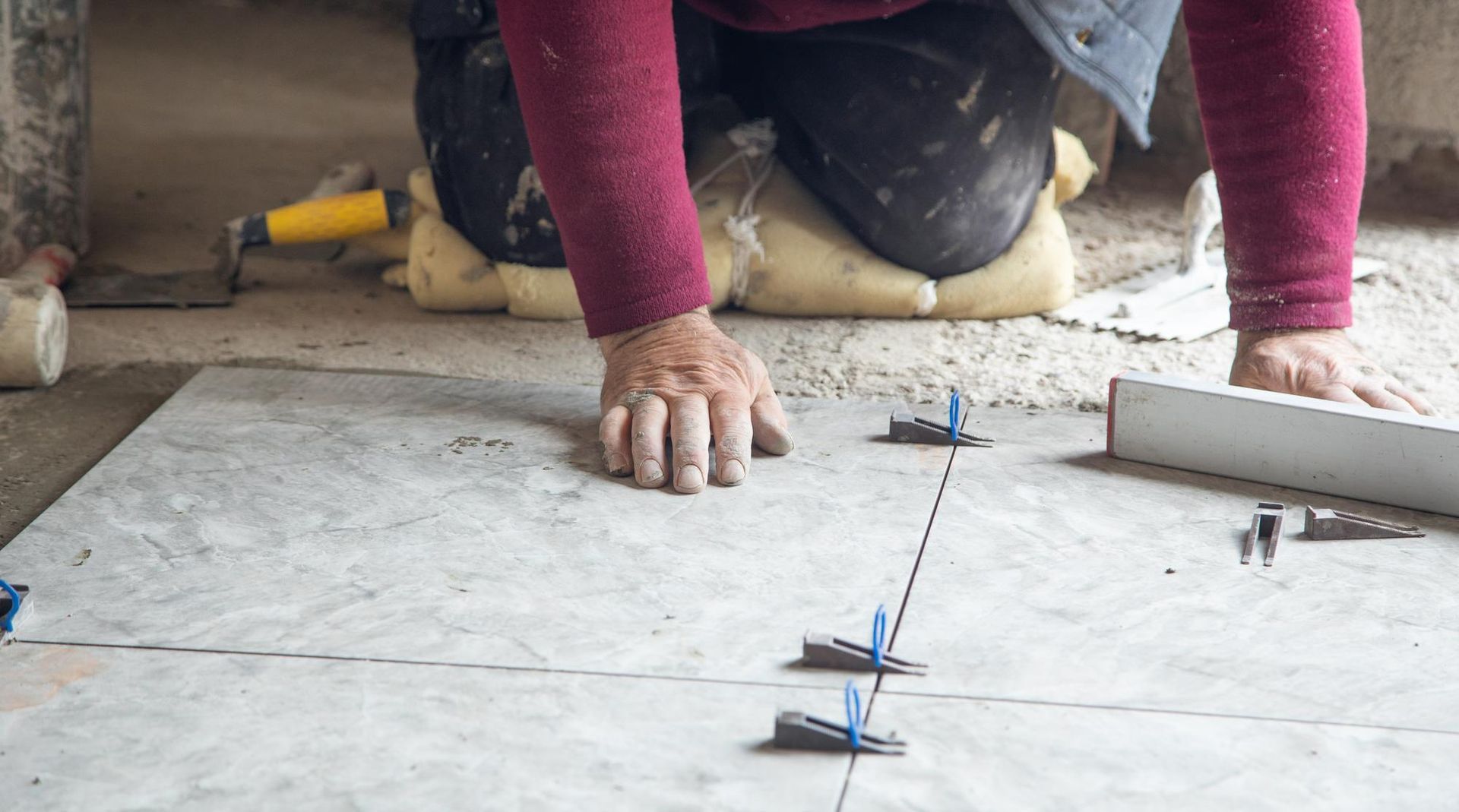 Worker aligning floor tiles with spacers and a trowel during installation work