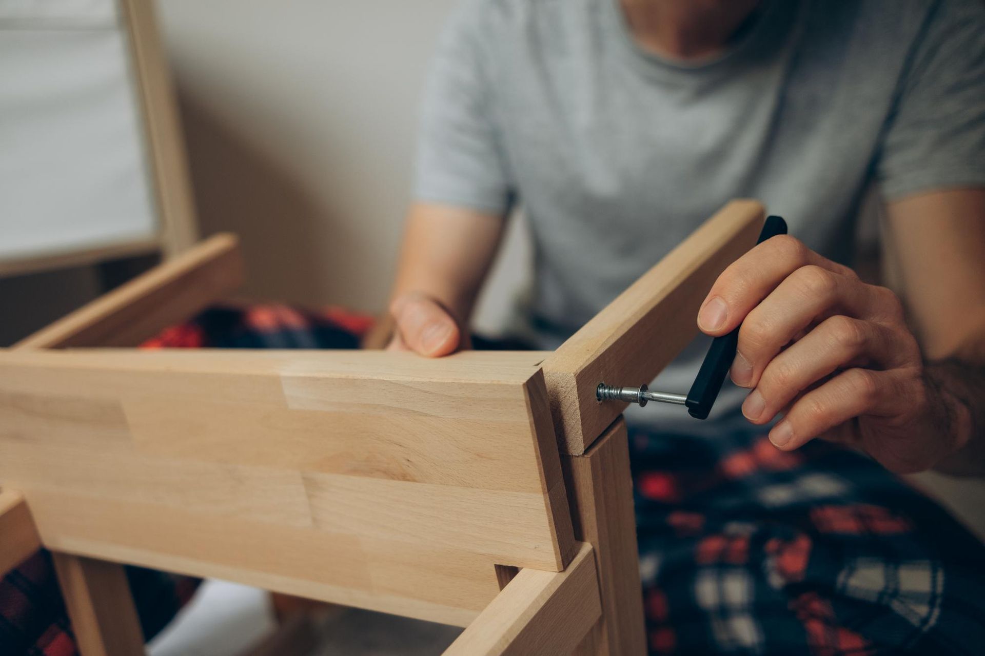 Person assembling a wooden chair with a screwdriver indoors