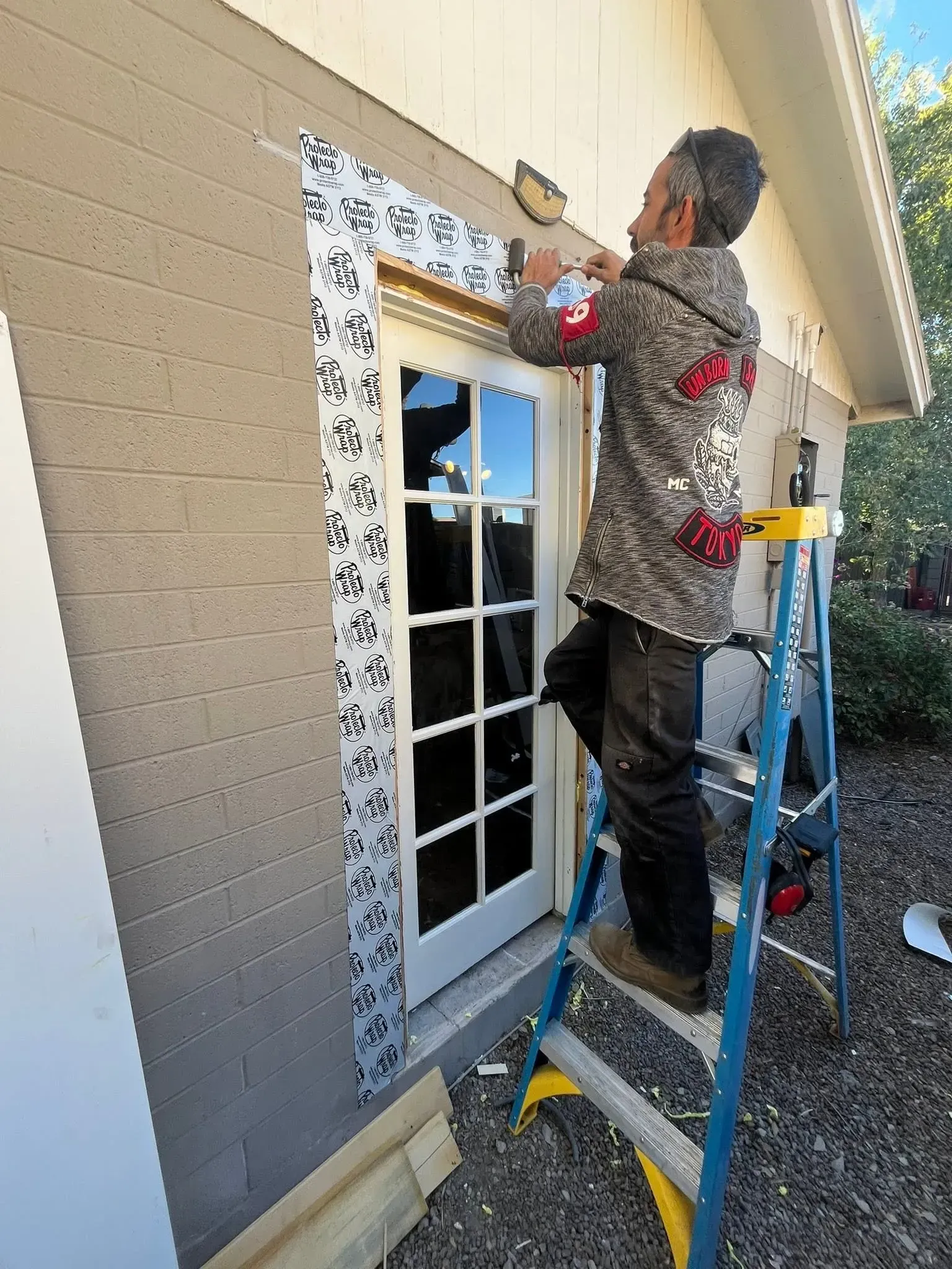 Person on a ladder installing trim around a window on a beige house exterior. Person on a ladder installing trim around a window on a beige house exterior.