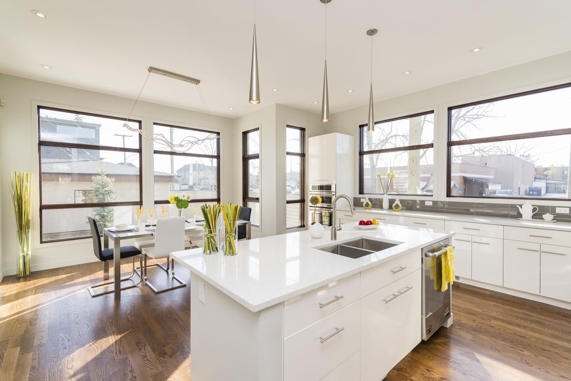 Bright modern kitchen with white island, pendant lights, large windows, and hardwood floors