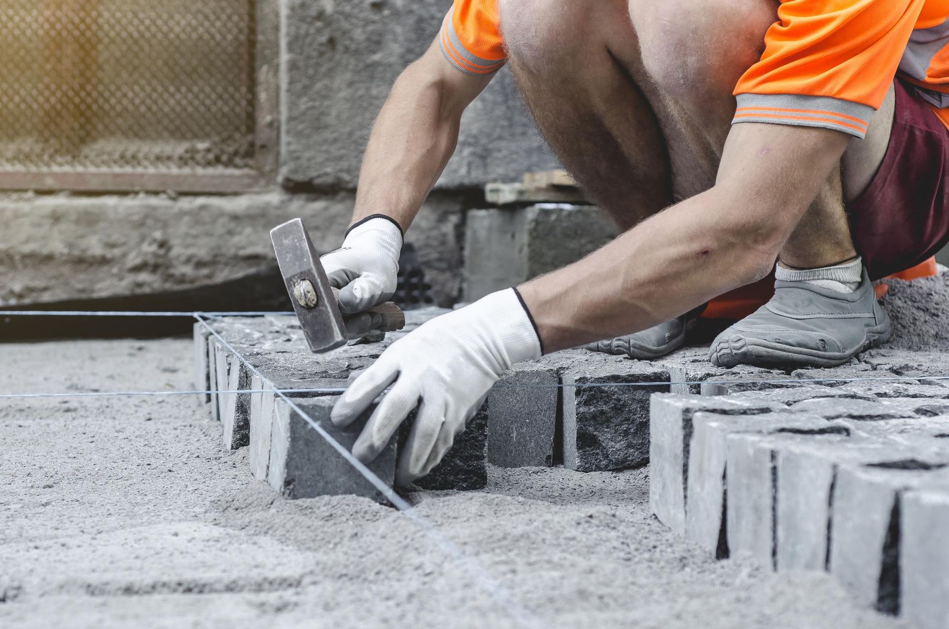Worker laying gray paving stones with a mallet and gloves on a construction site