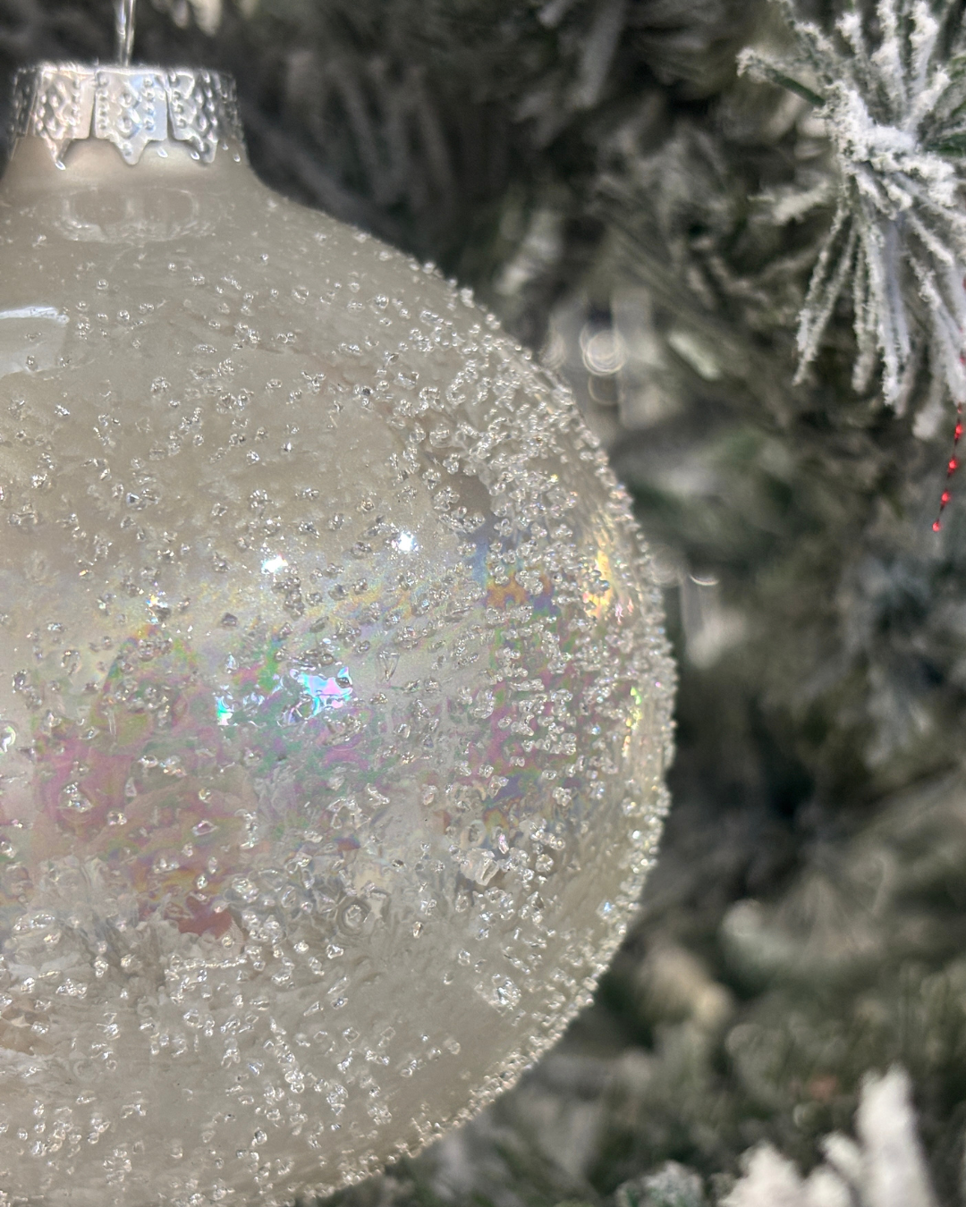 Close-up of a sparkling white Christmas ornament hanging on a frosted Christmas tree.