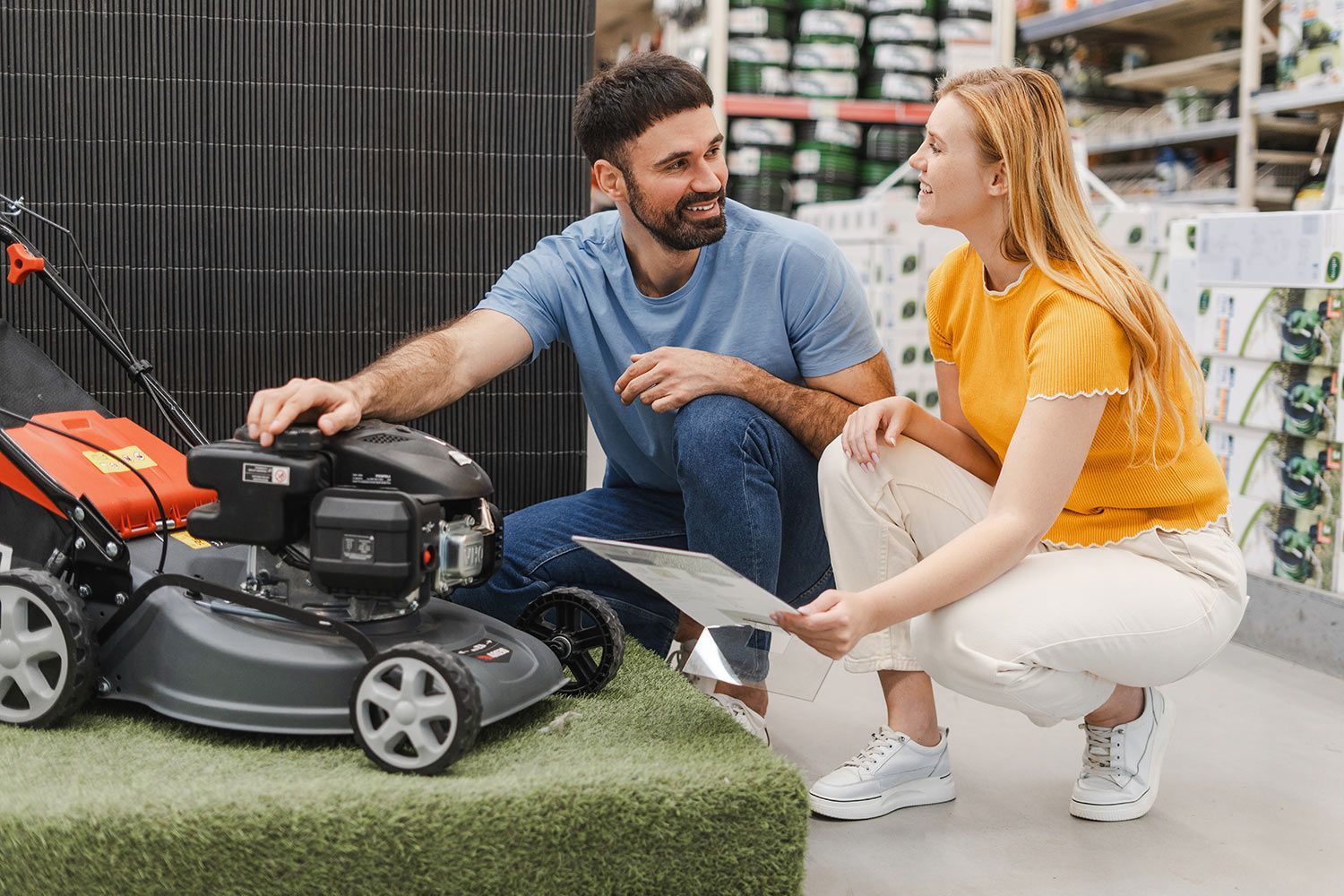 Two people examine a lawn mower together inside a home improvement store. Two people examine a lawn mower together inside a home improvement store.