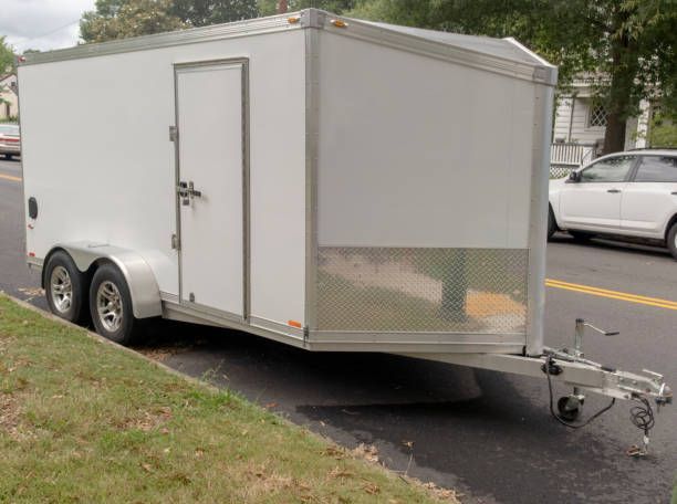 A white trailer is parked on the side of the road next to a white car.