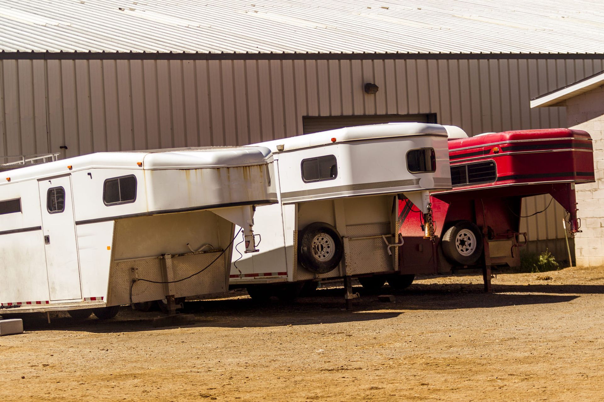 Two horse trailers are parked next to each other in front of a building.