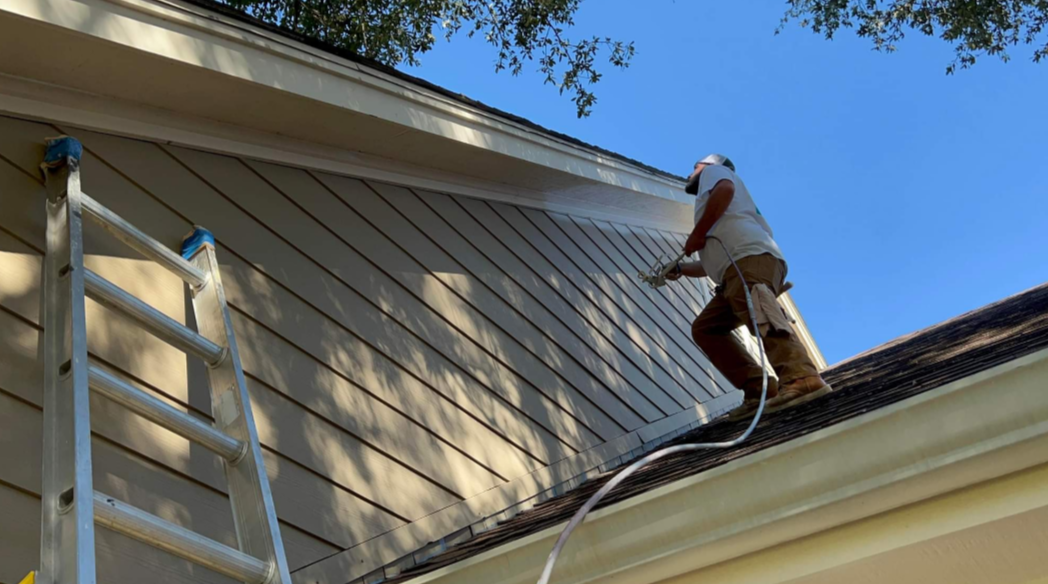 A man is spraying paint on the side of a house.