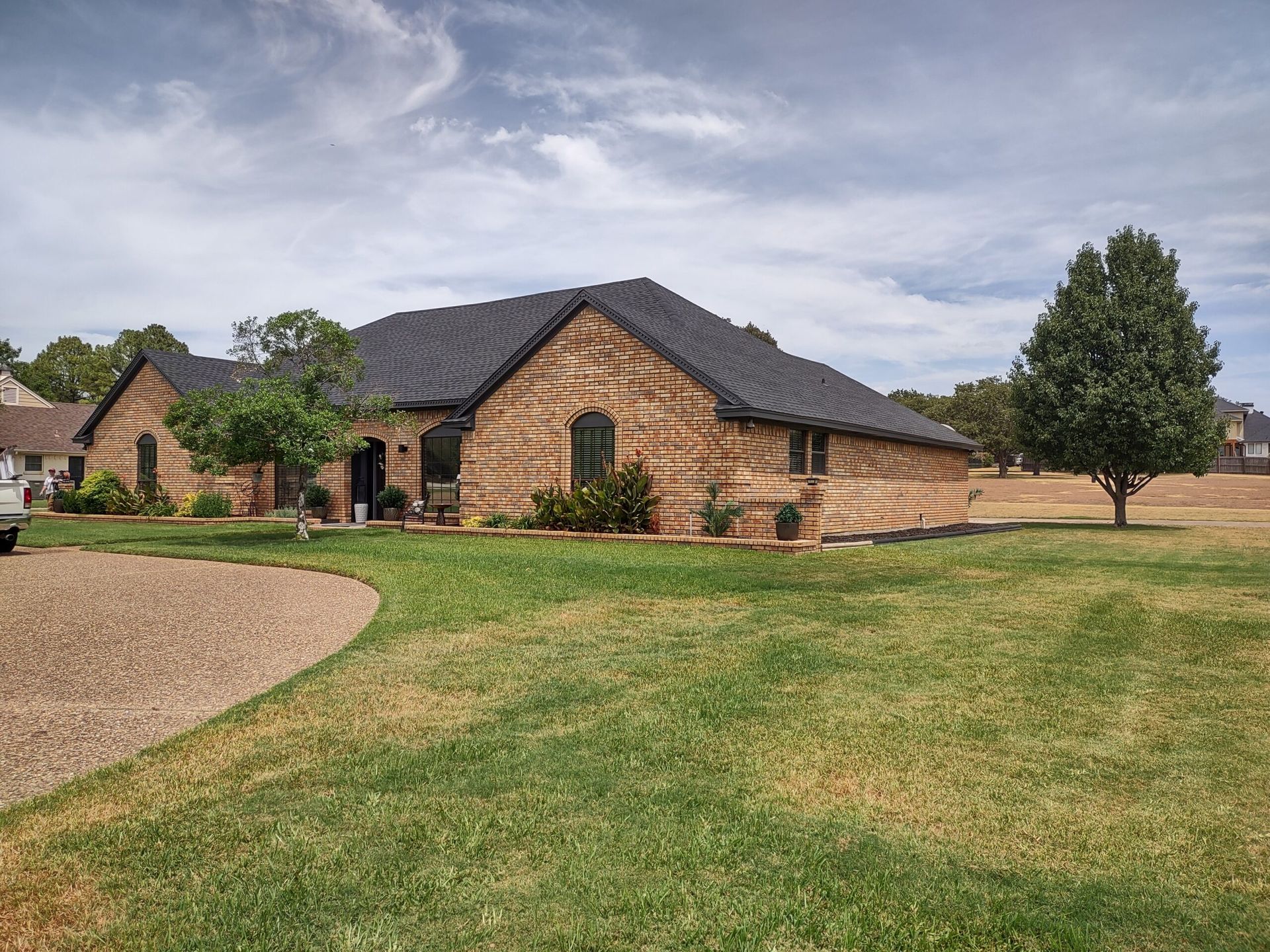 A large brick house with a black roof is sitting on top of a lush green field.