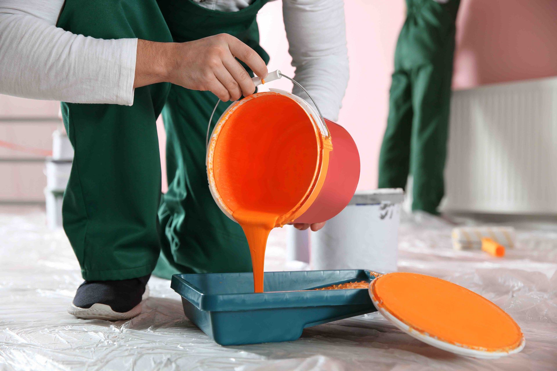 A person is pouring orange paint into a tray.
