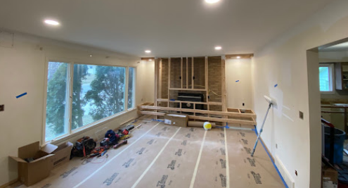 Renovation in progress in a living room with exposed wall framing, tools, and protective floor covering.