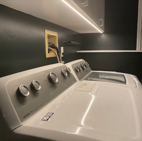 Modern laundry room with white washer and dryer under dark walls and under-cabinet lighting