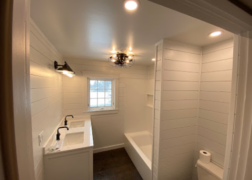 Bright white bathroom with a sink, bathtub, toilet, and shiplap walls under recessed lights.