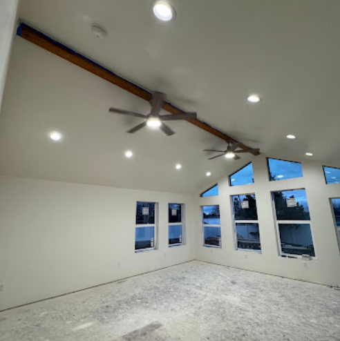 Spacious unfinished room with white walls, recessed lights, ceiling fans, and large windows.