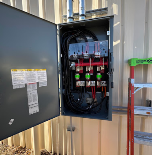 Open electrical control panel with wiring and breakers mounted on a wall.