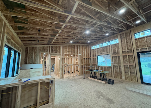 Framed house interior under construction with exposed rafters, insulation, windows, and workbenches