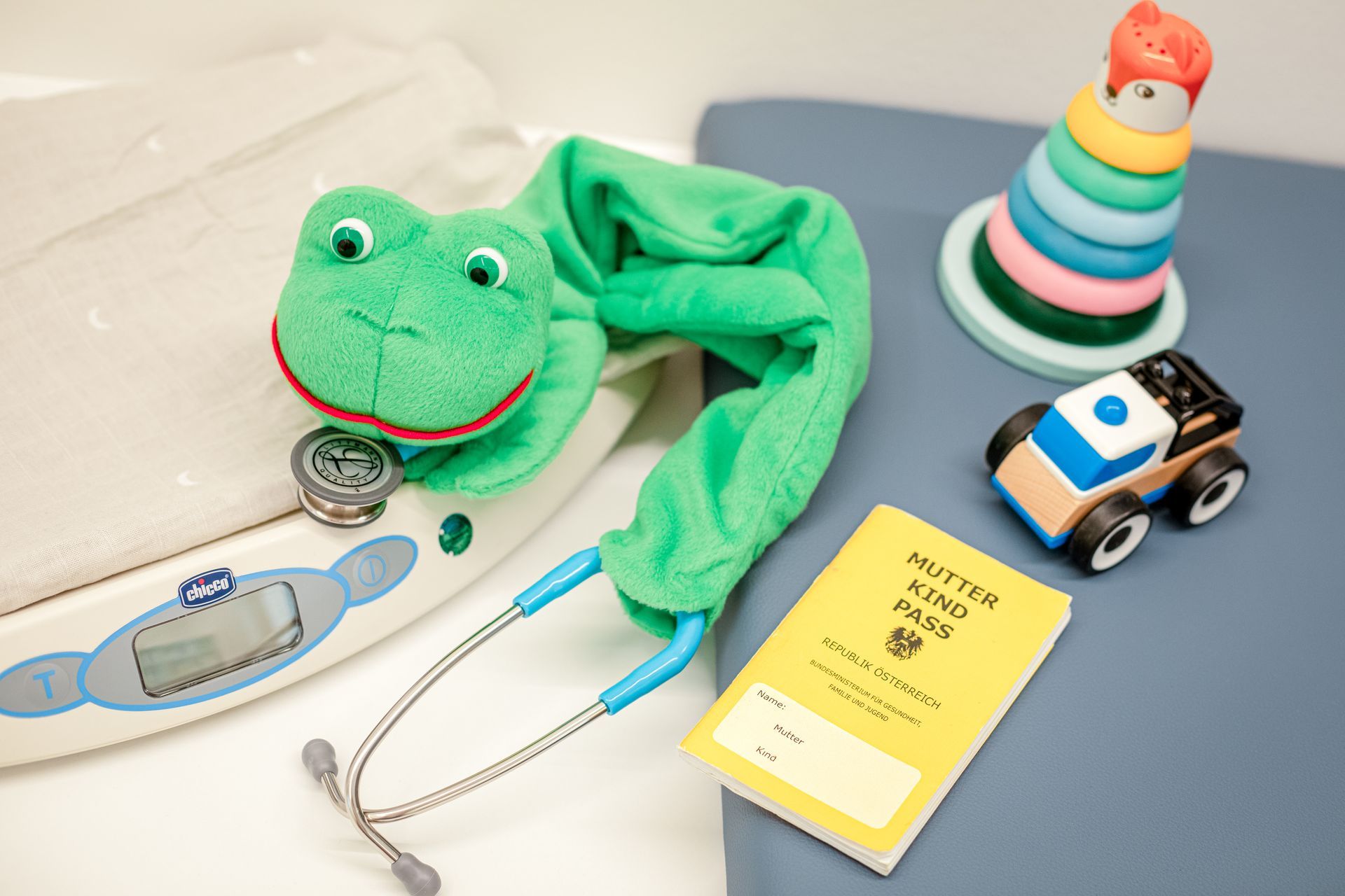Ein Stofffrosch sitzt auf einer Waage neben einem Stethoskop