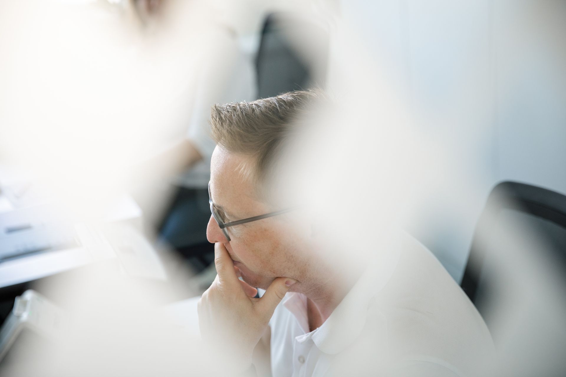 Ein Mann mit Brille sitzt an einem Schreibtisch und legt die Hand auf sein Kinn.