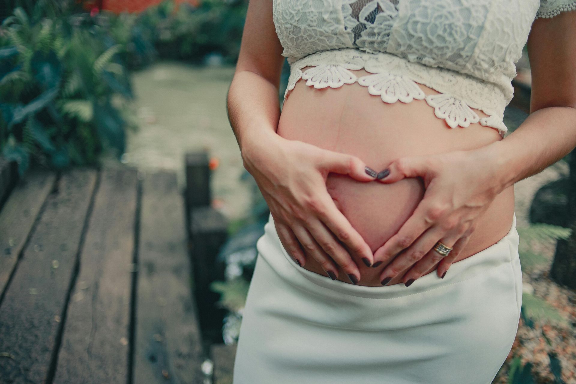 Eine schwangere Frau formt mit ihren Händen auf ihrem Bauch ein Herz.