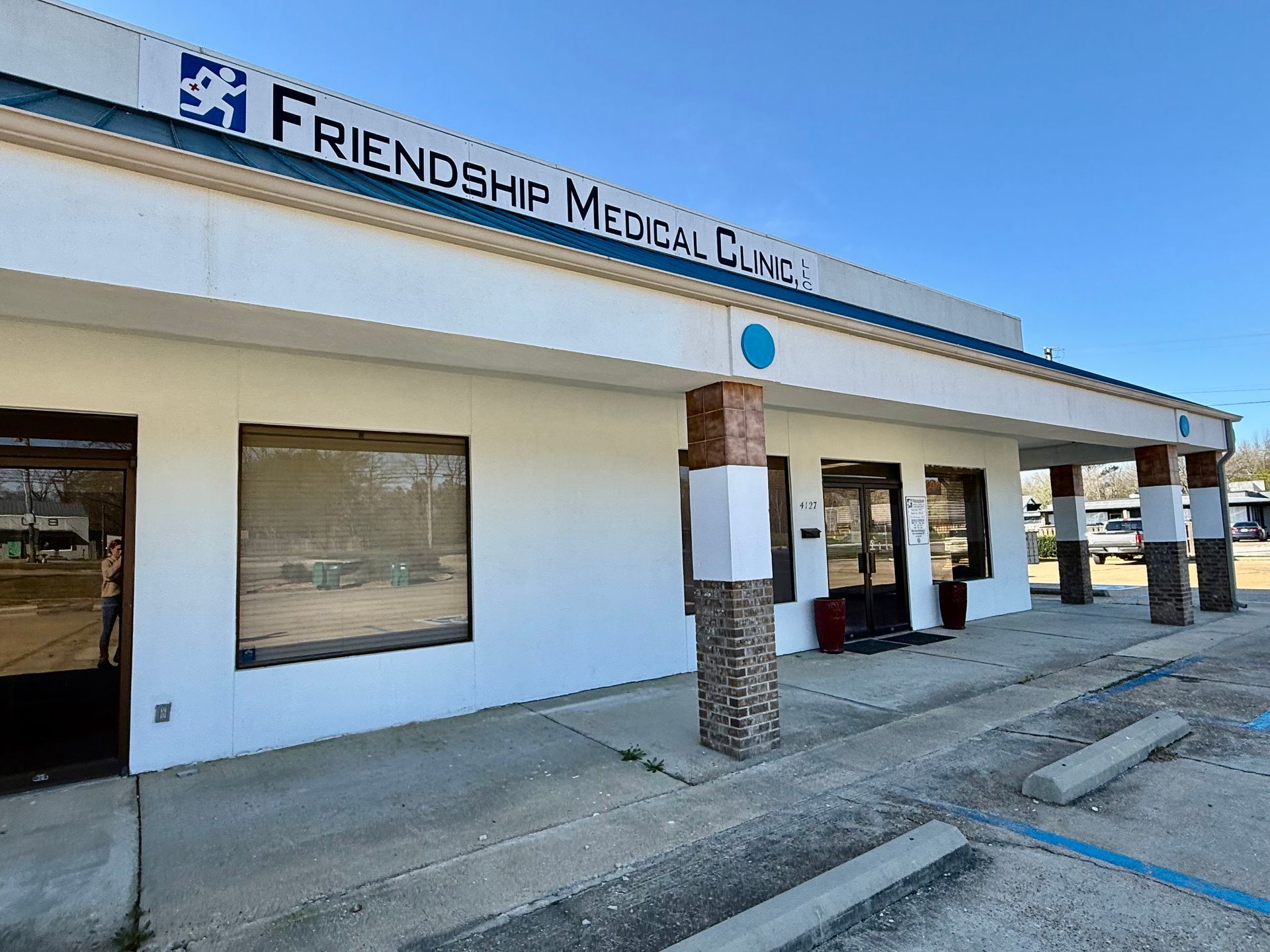 The white exterior of Friendship Medical Clinic under a clear blue sky, featuring a covered entrance with stone pillars.