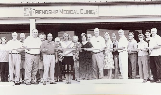 A group of people standing in front of Friendship Medical Clinic, participating in a ribbon-cutting ceremony.