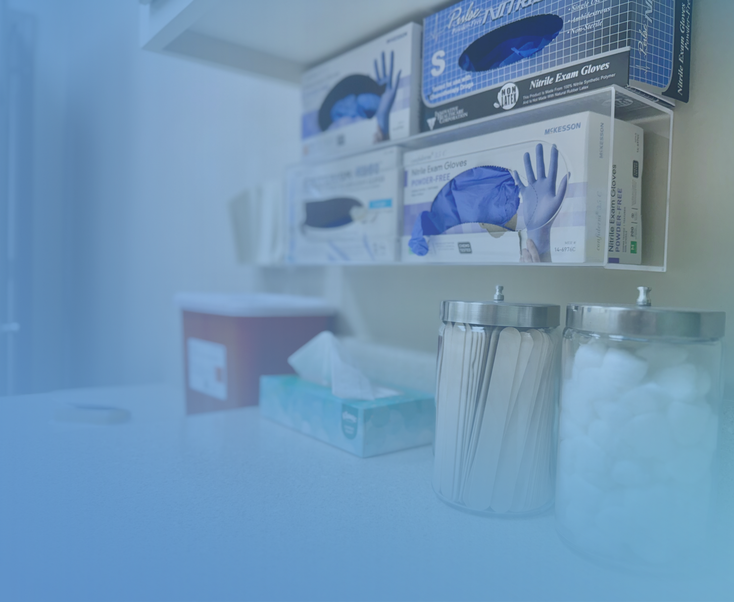 Supplies on a counter including boxes of gloves, a tissue box, a sharps container, and jars of swabs and cotton balls.