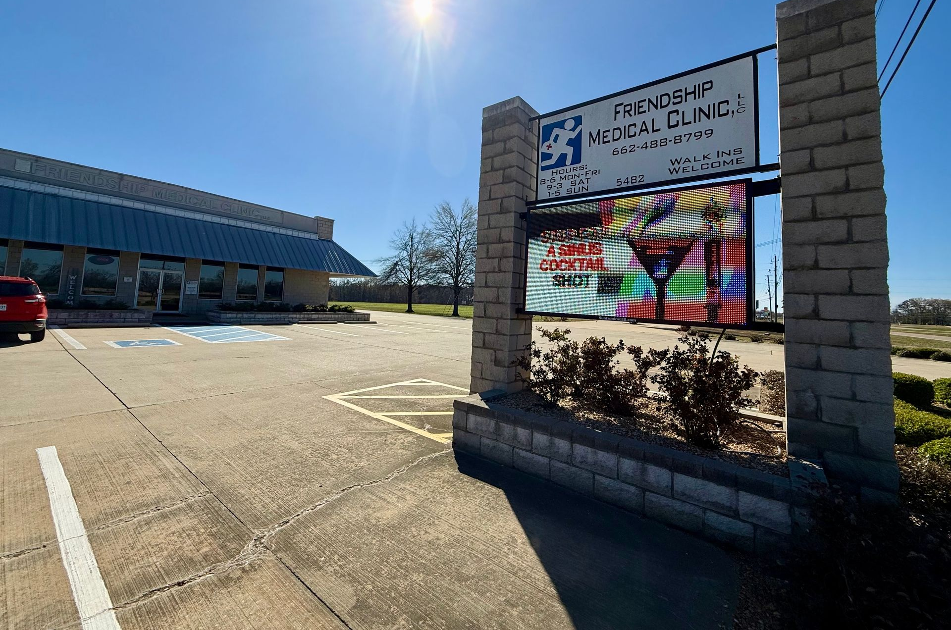 A sunny parking lot with a brick sign for a medical clinic featuring a colorful banner that reads