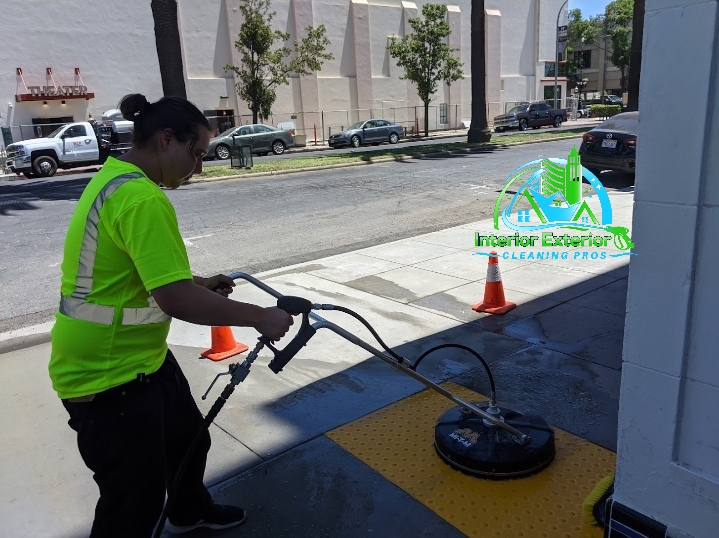 A woman in a neon green shirt is cleaning a sidewalk with a machine.