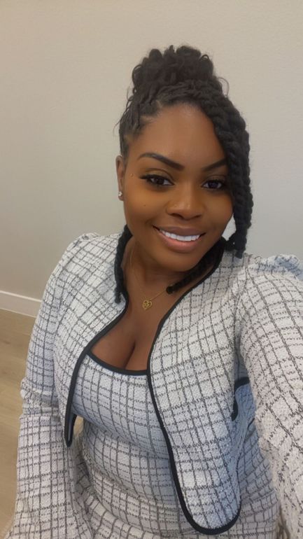 Smiling person in a light plaid jacket and top, posing indoors against a plain wall.