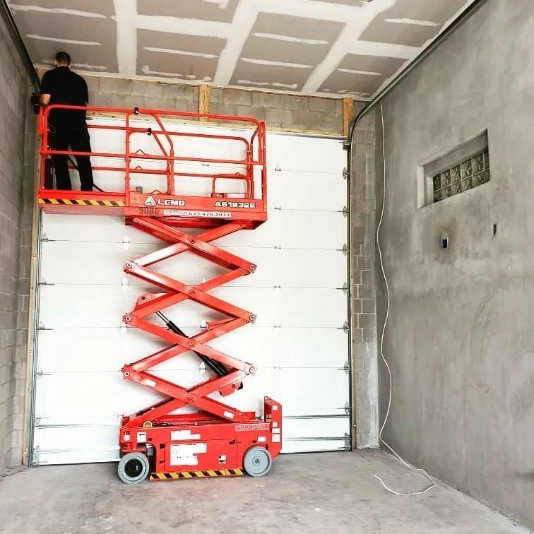 A technician is using a red scissor lift to install a white garage door in a newly constructed garag